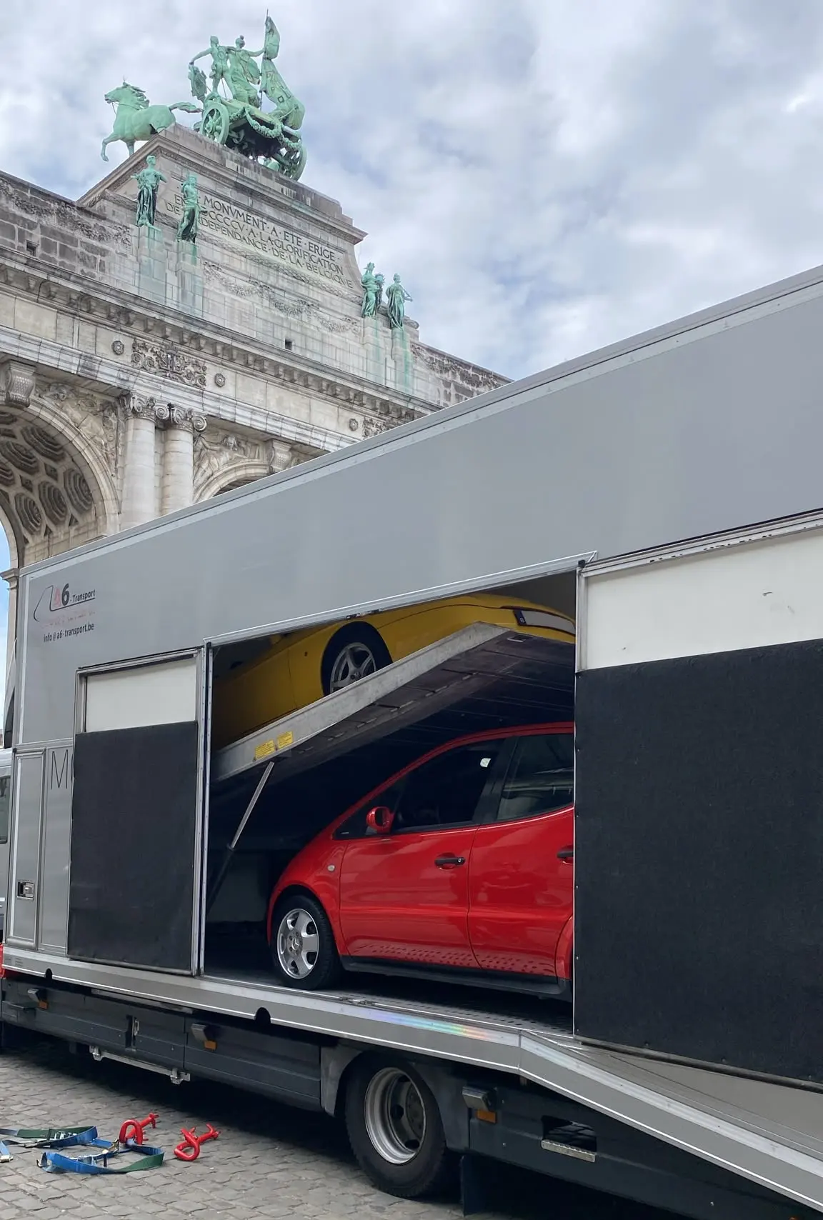 Camion fermé chargé d'une voiture rouge devant l'arc du Cinquantenaire