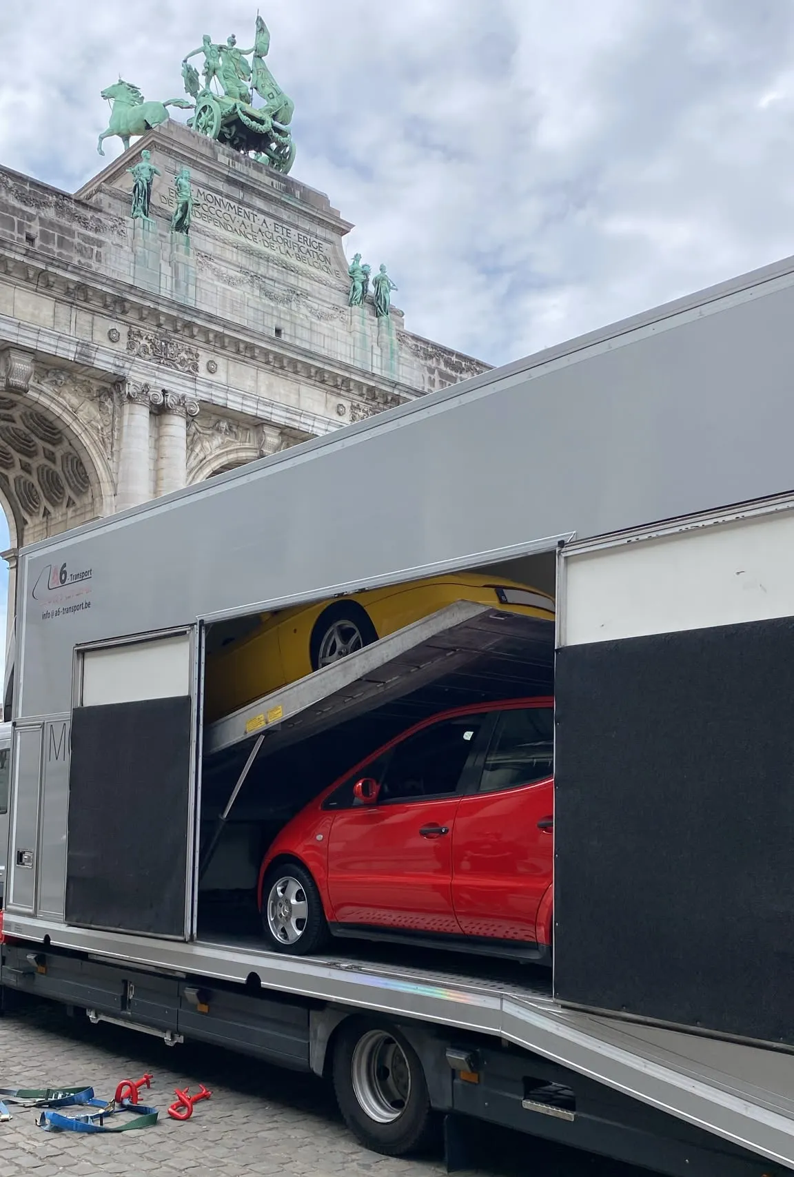 Gesloten transporter geladen met een rode wagen bij de Jubelparkboog