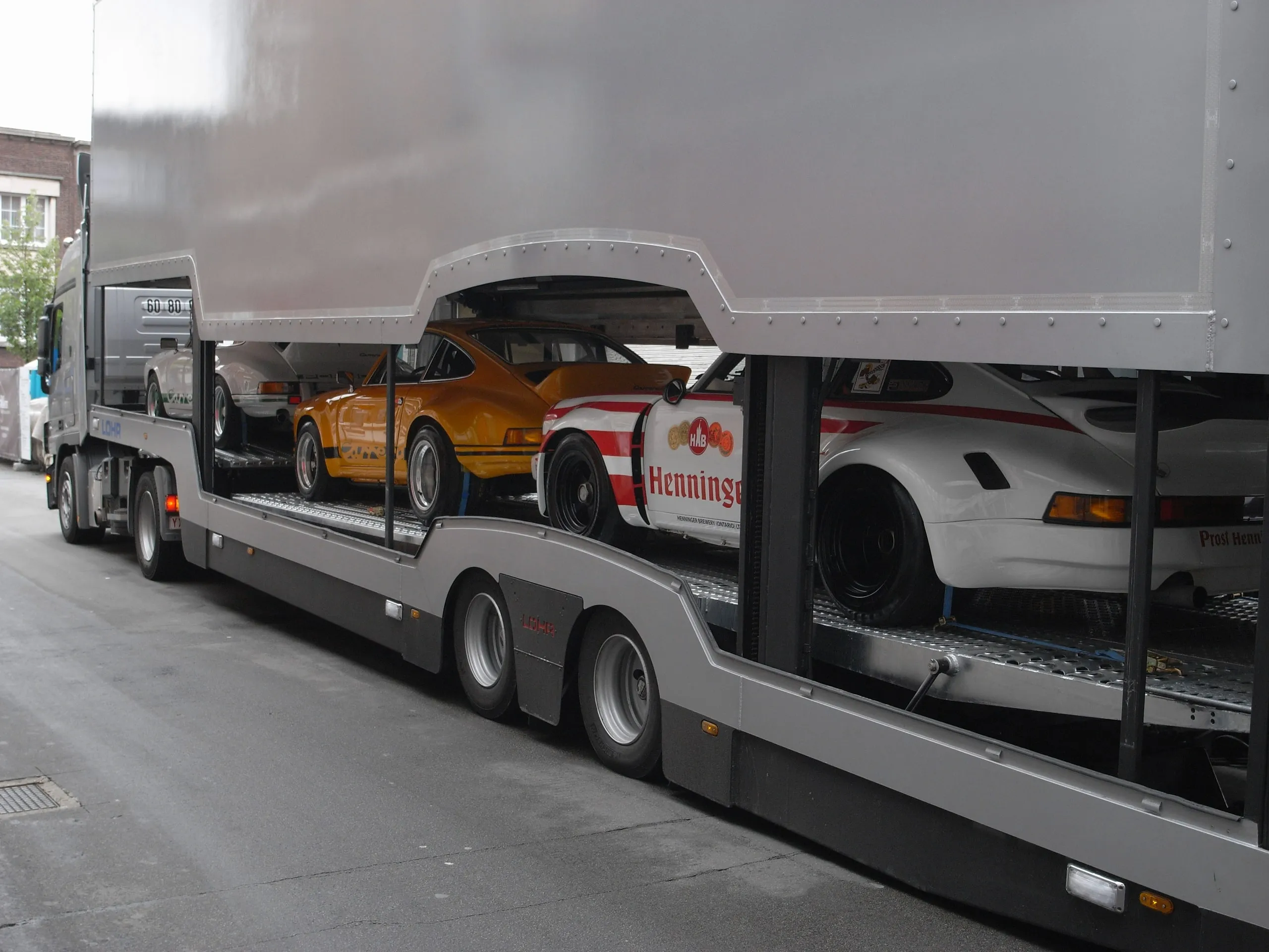 Flanke eines beladenen Transporters, Porsche 911 zwischen den Decks sichtbar