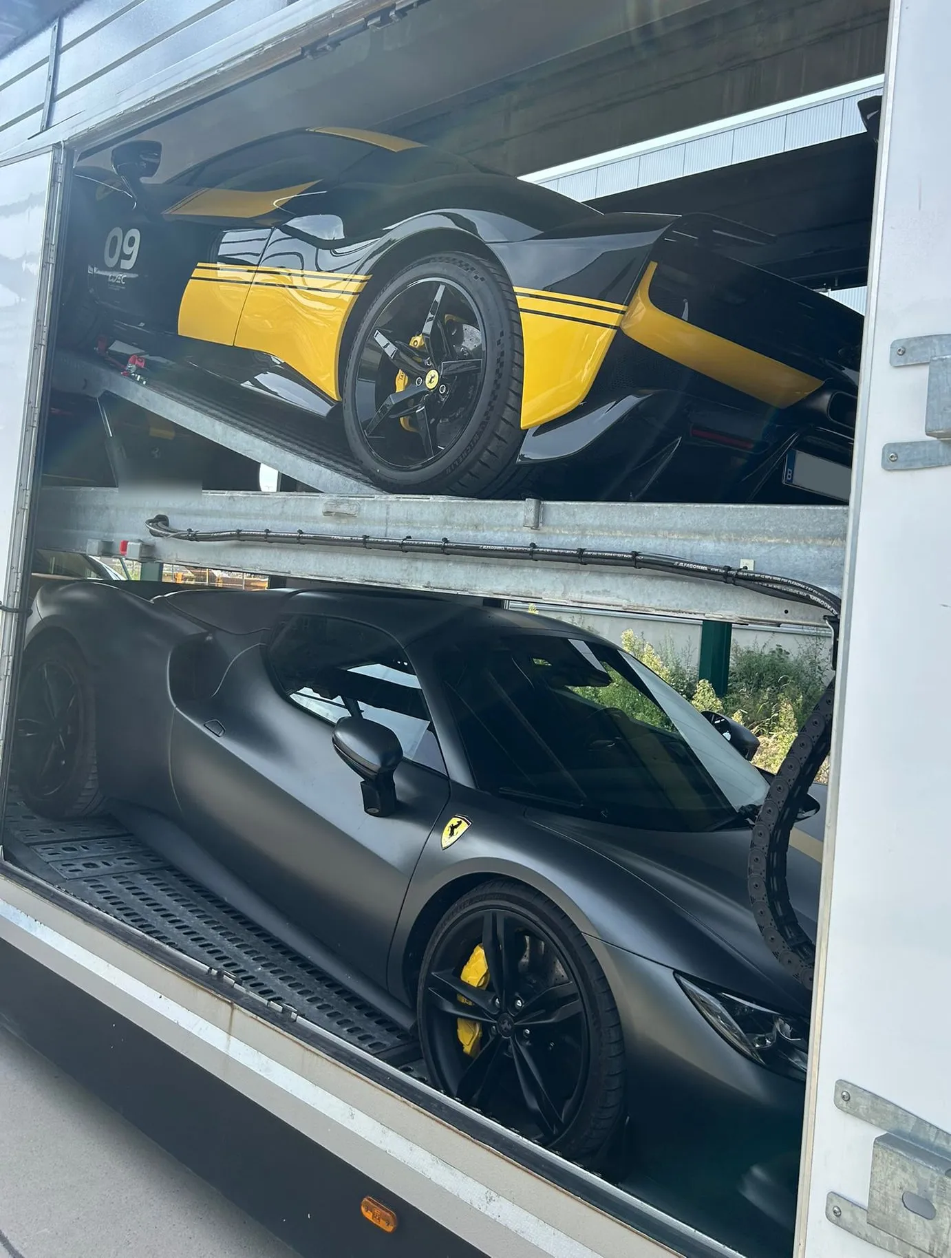 Zwarte Ferrari met gele banen op het bovendek, gezien door de open zijdeur, matzwarte Ferrari eronder