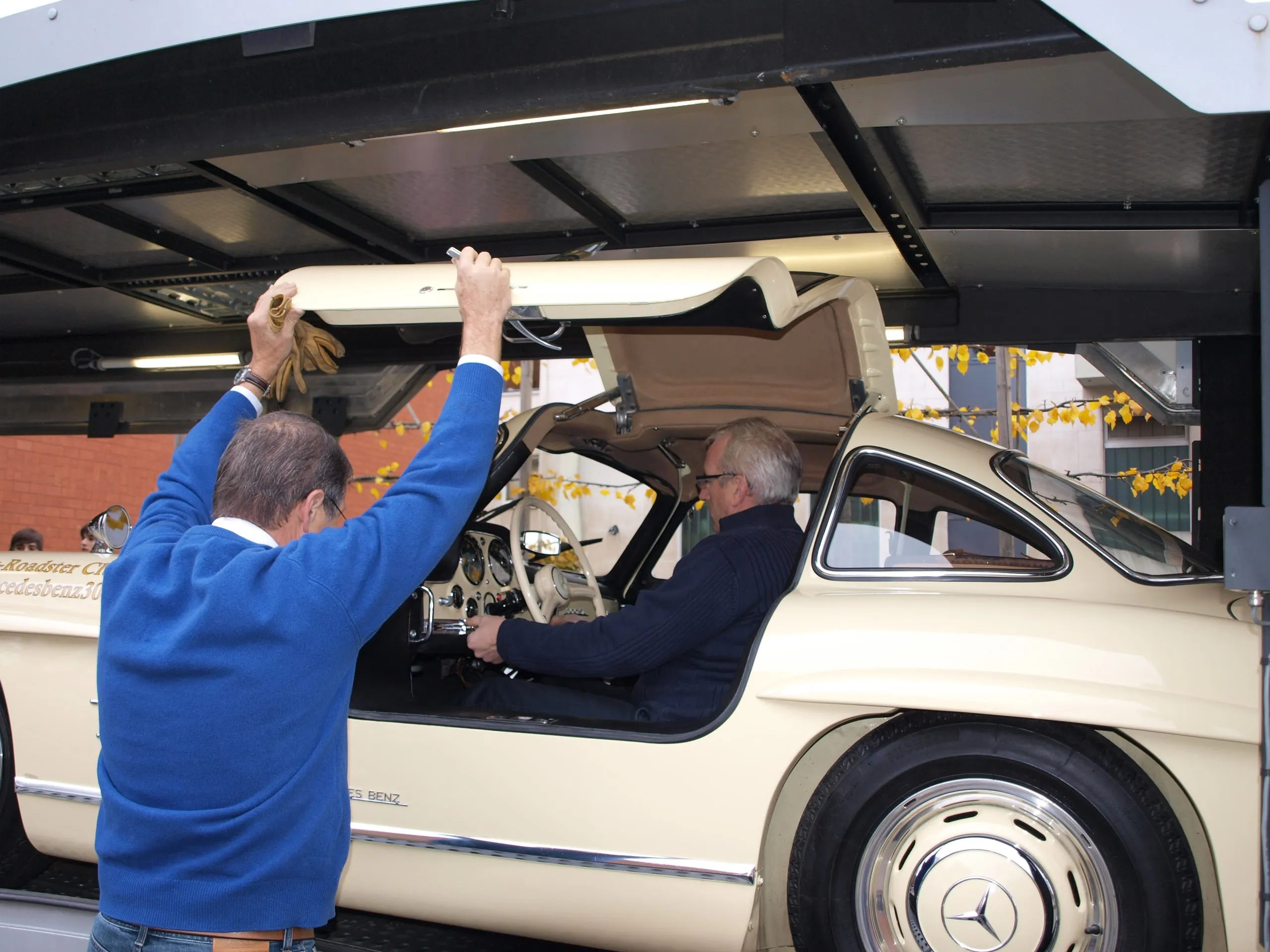 Twee crewleden sluiten de vleugeldeur van een Mercedes 300 SL