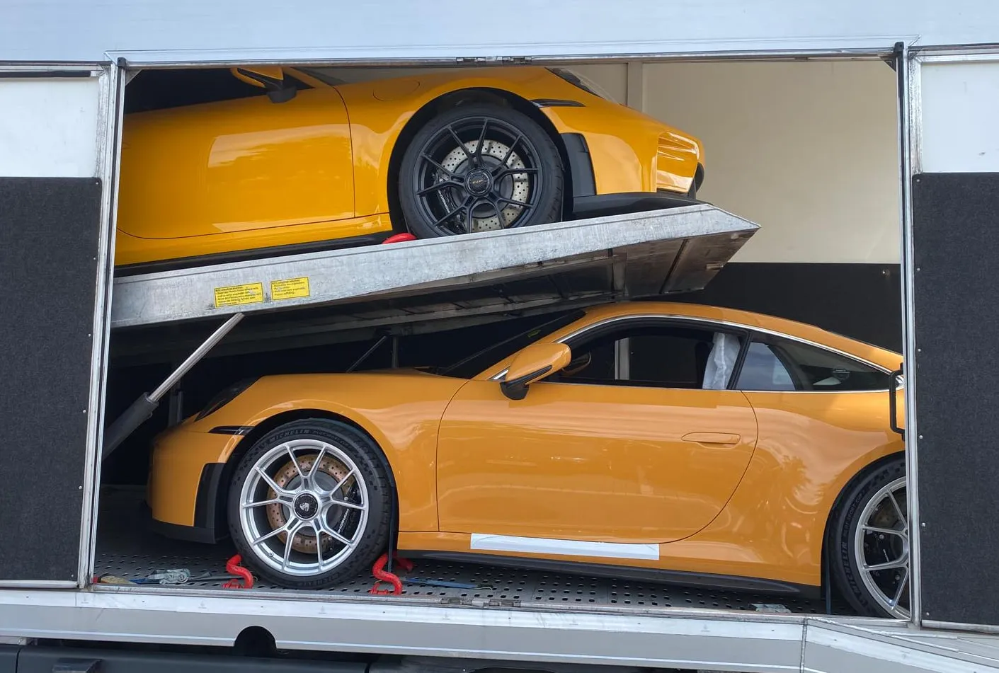 Twee oranje Porsche 911 GT3's op beide dekken van een transporter