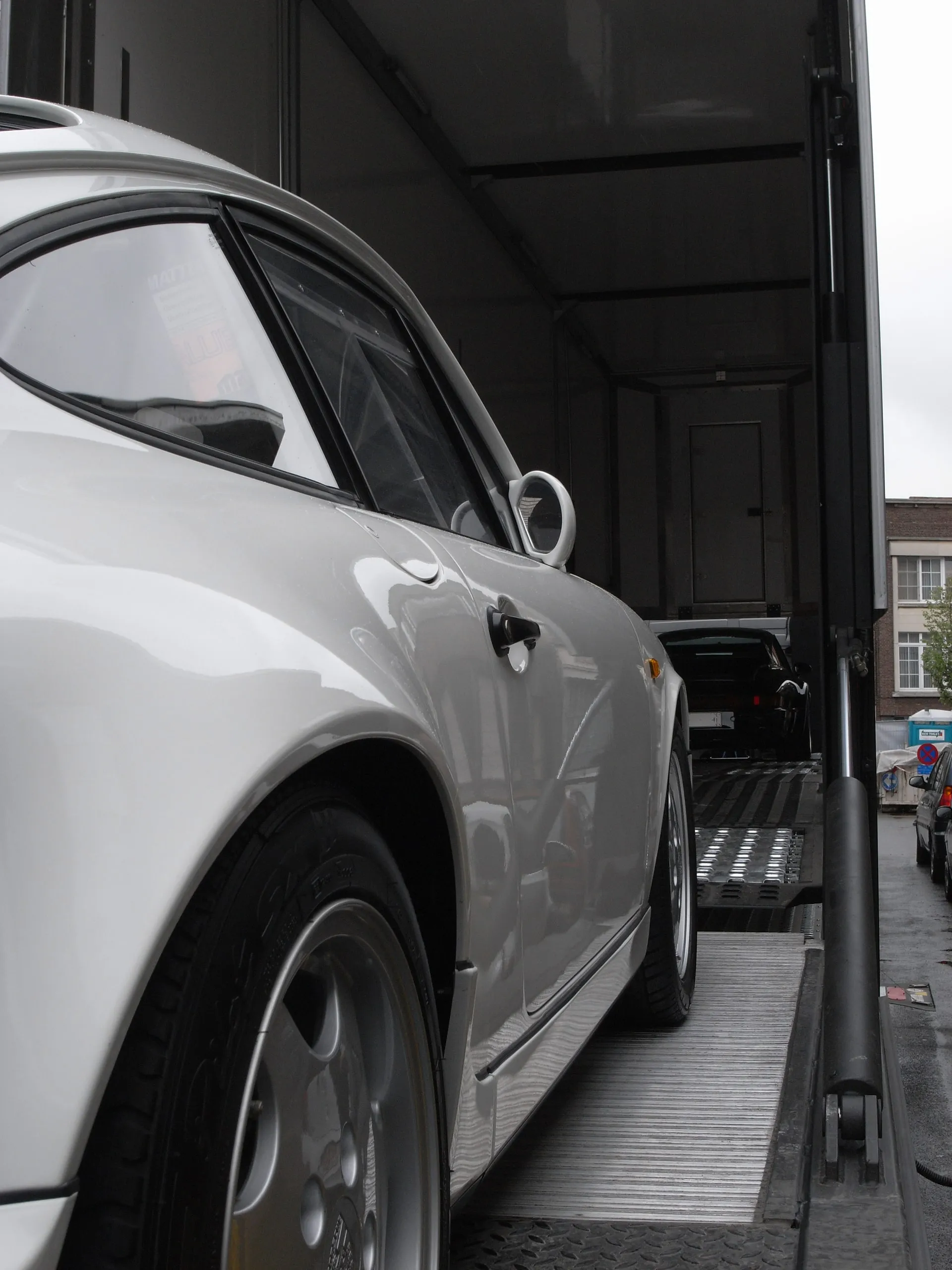 Witte Porsche 911 geladen in een gesloten transporter, de straat erachter zichtbaar