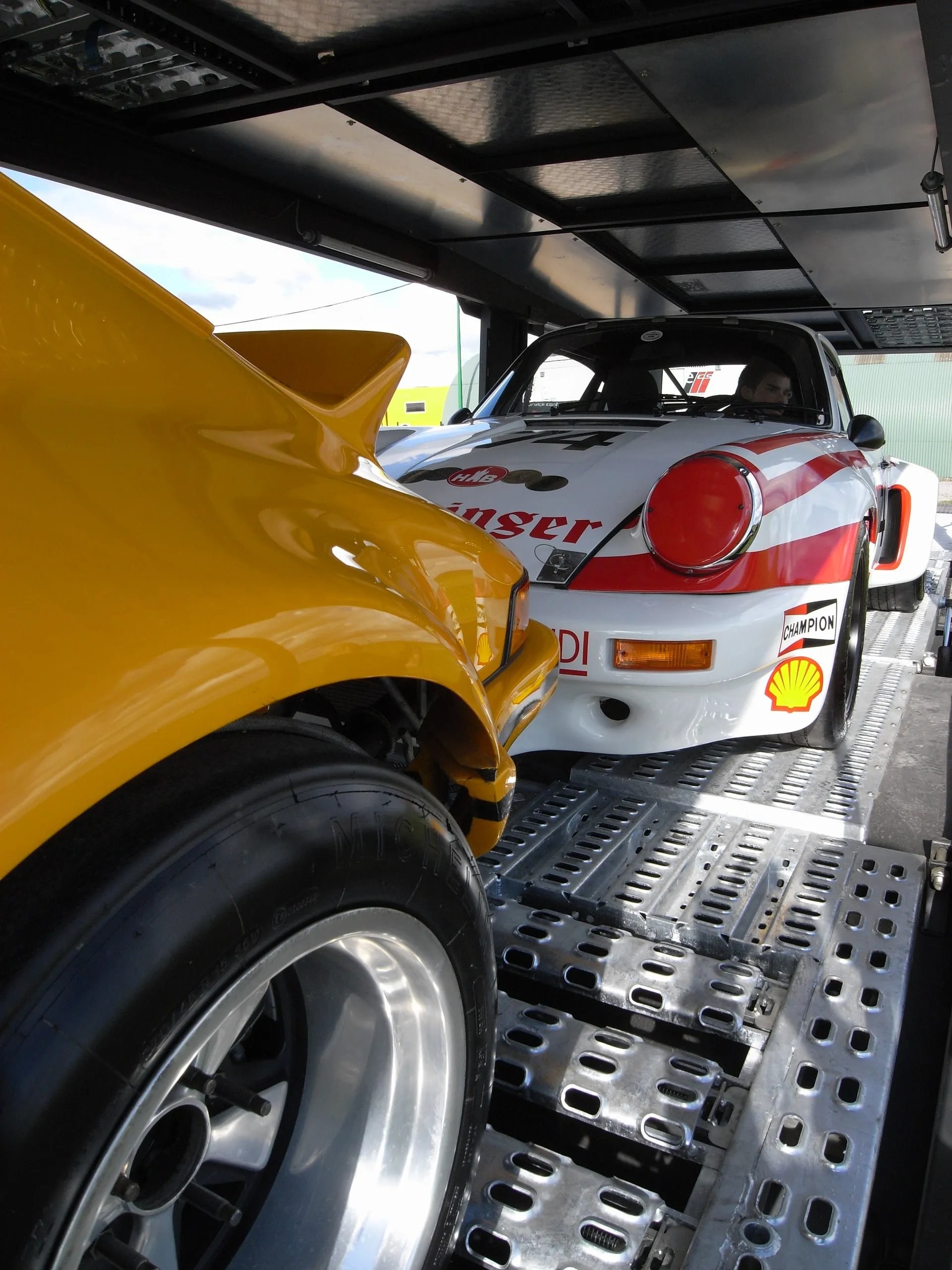 Gele Porsche 911 en een exemplaar in racekleuren naast elkaar op het dek