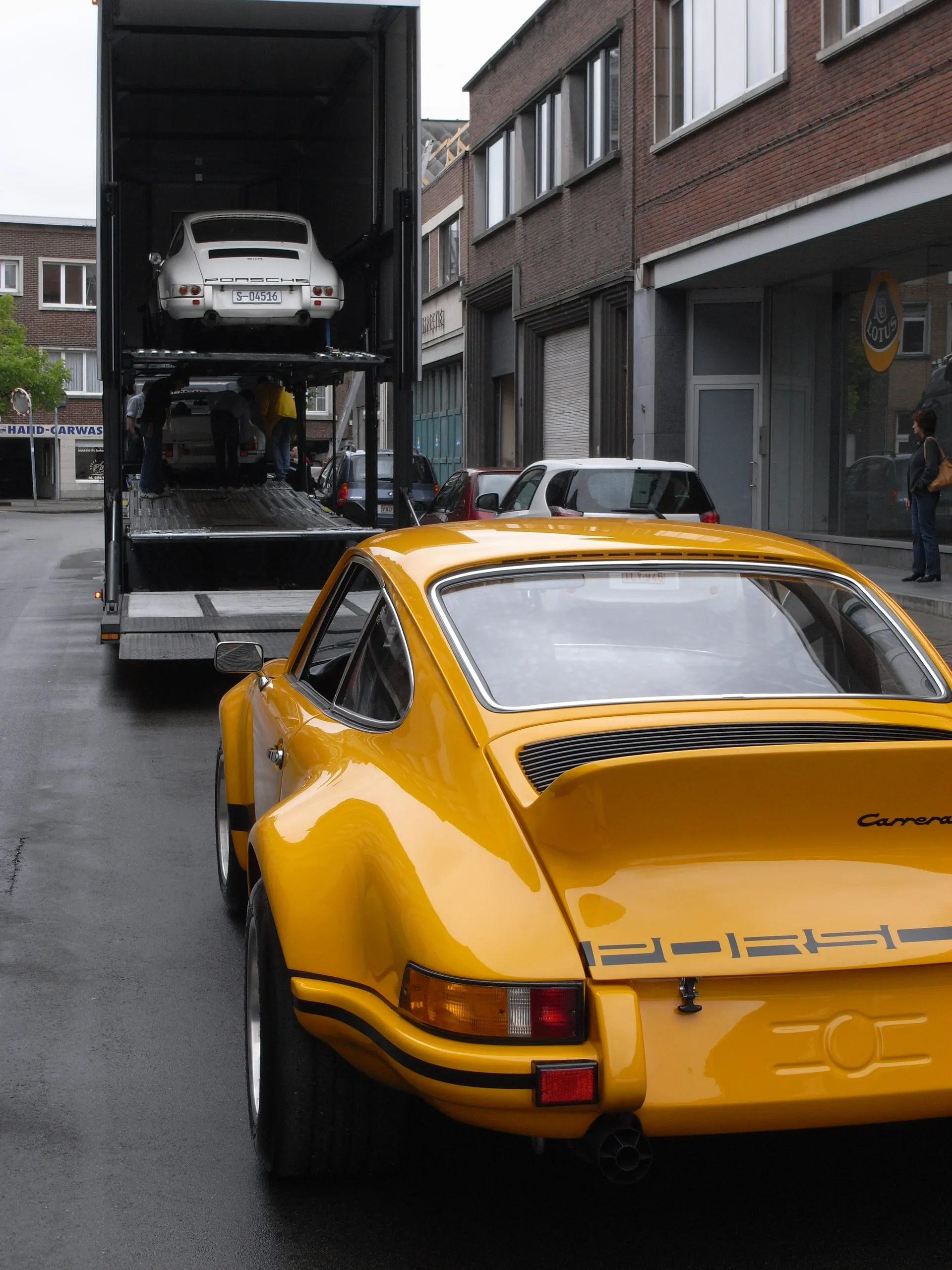 Gele Porsche 911 Carrera RS in een straat, de geladen transporter erachter