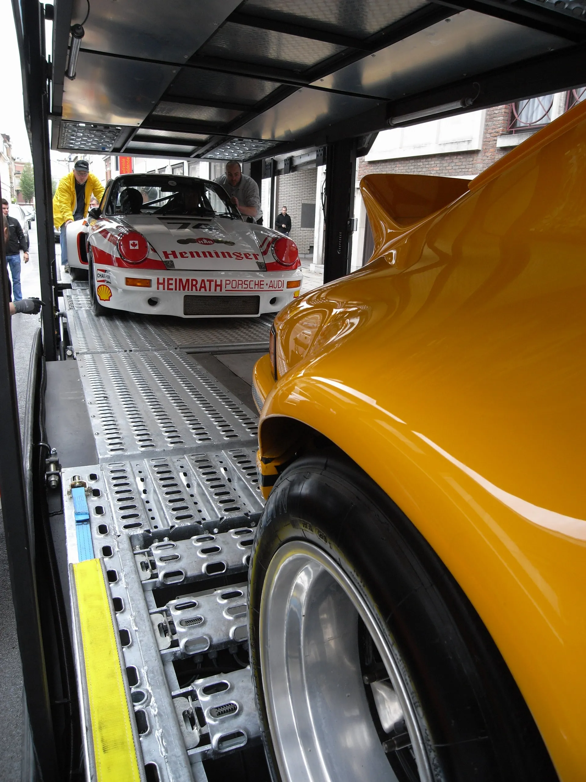 Flank van een gele Porsche 911, verderop op het dek een 911 in racekleuren