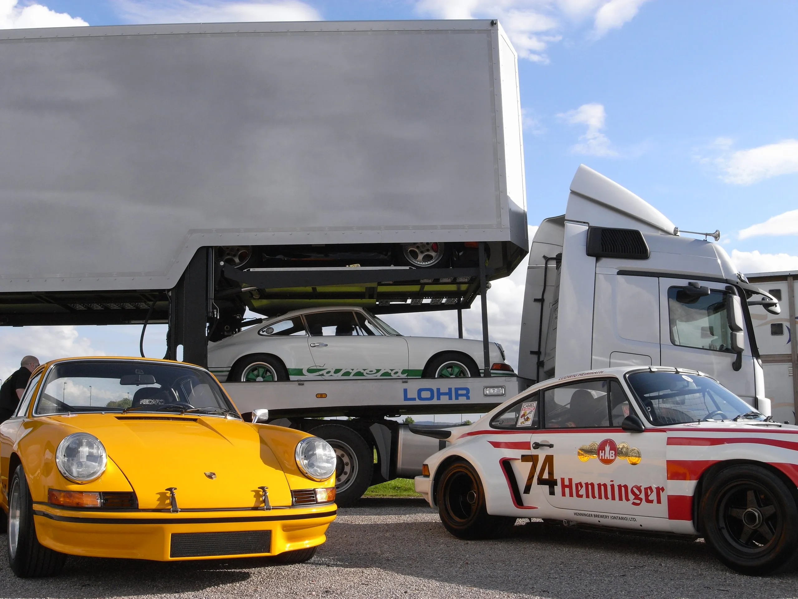Gele Porsche 911 RS en een race-911 geparkeerd naast de geladen transporter