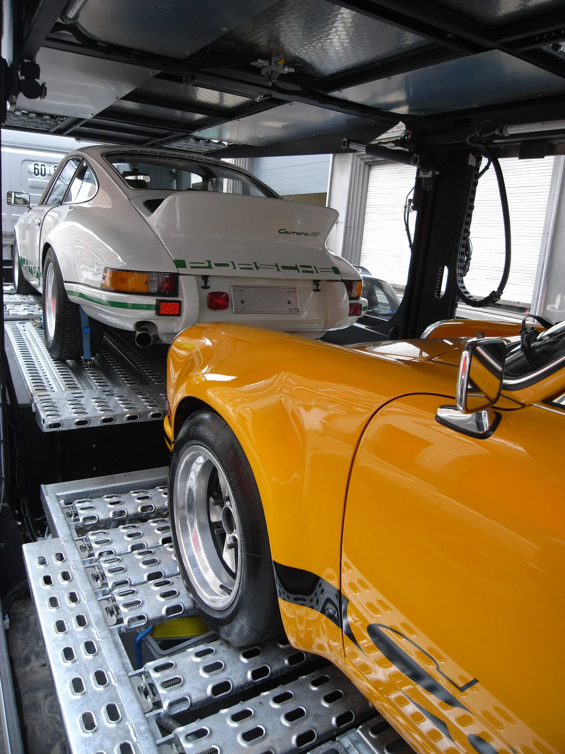 Gele Porsche 911 RS op het onderdek en een witte 911 op het bovendek