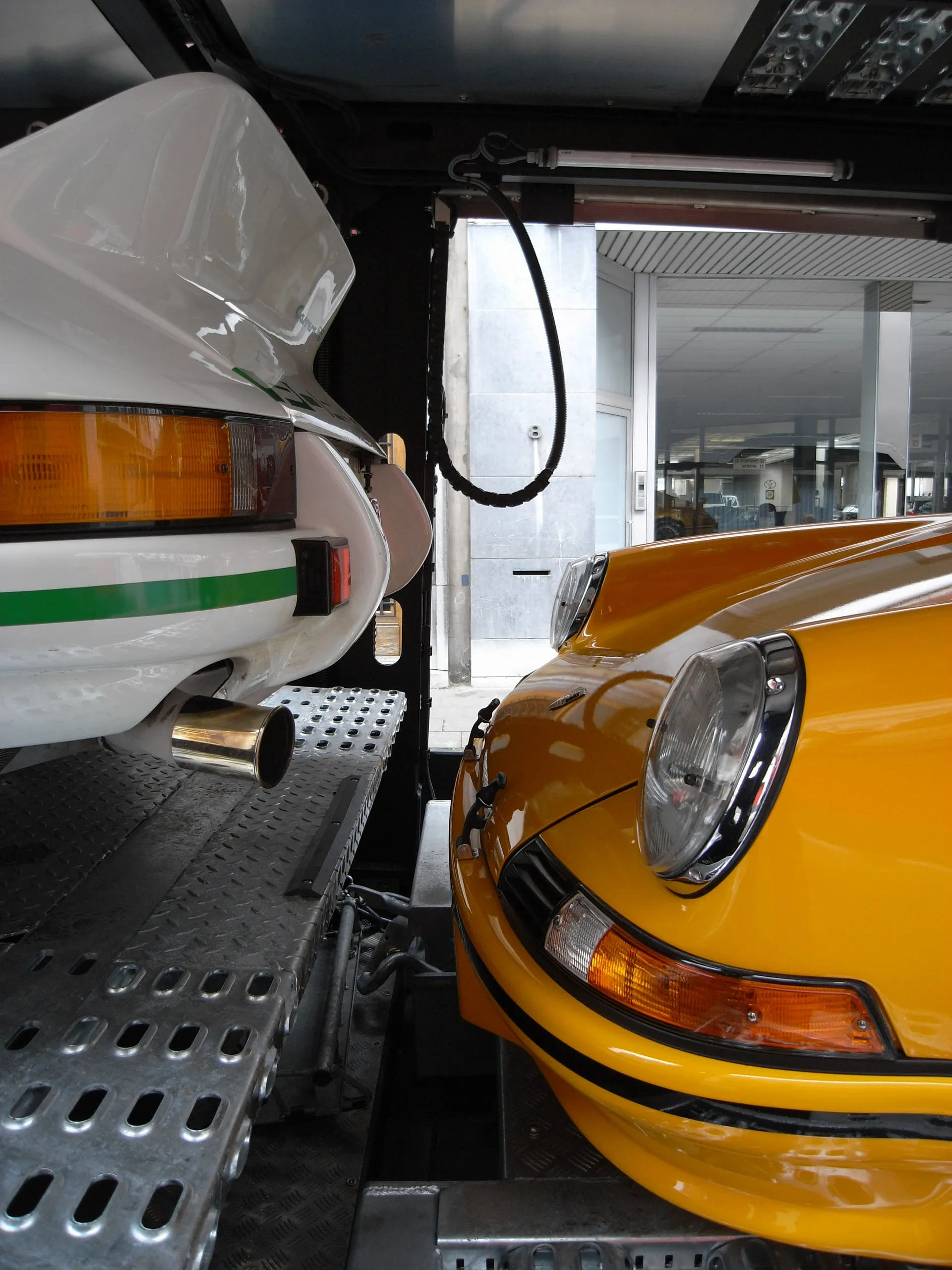 Neus van een gele Porsche 911 RS naast een witte met groene streep op het dek